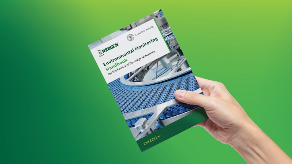 Hand holding the second edition of the Neogen Environmental Monitoring Handbook.