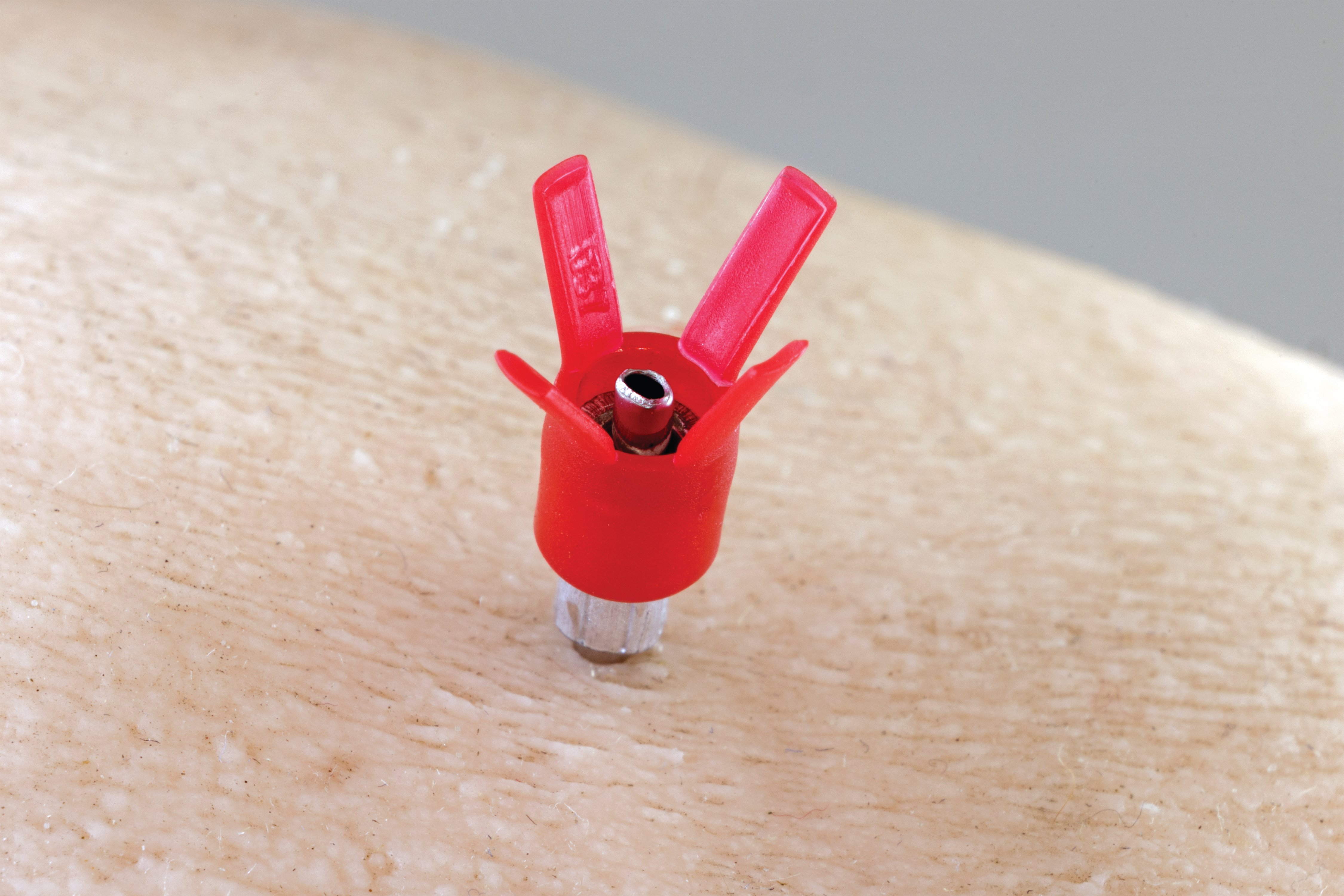 Close-up of a D3X™ needle in use, showing the red X-shaped plastic hub clearly visible against the skin.