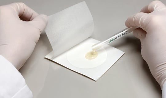 A lab technician applies a Neogen® Petrifilm® Rapid Plate on a pipe to test for environmental contamination.
