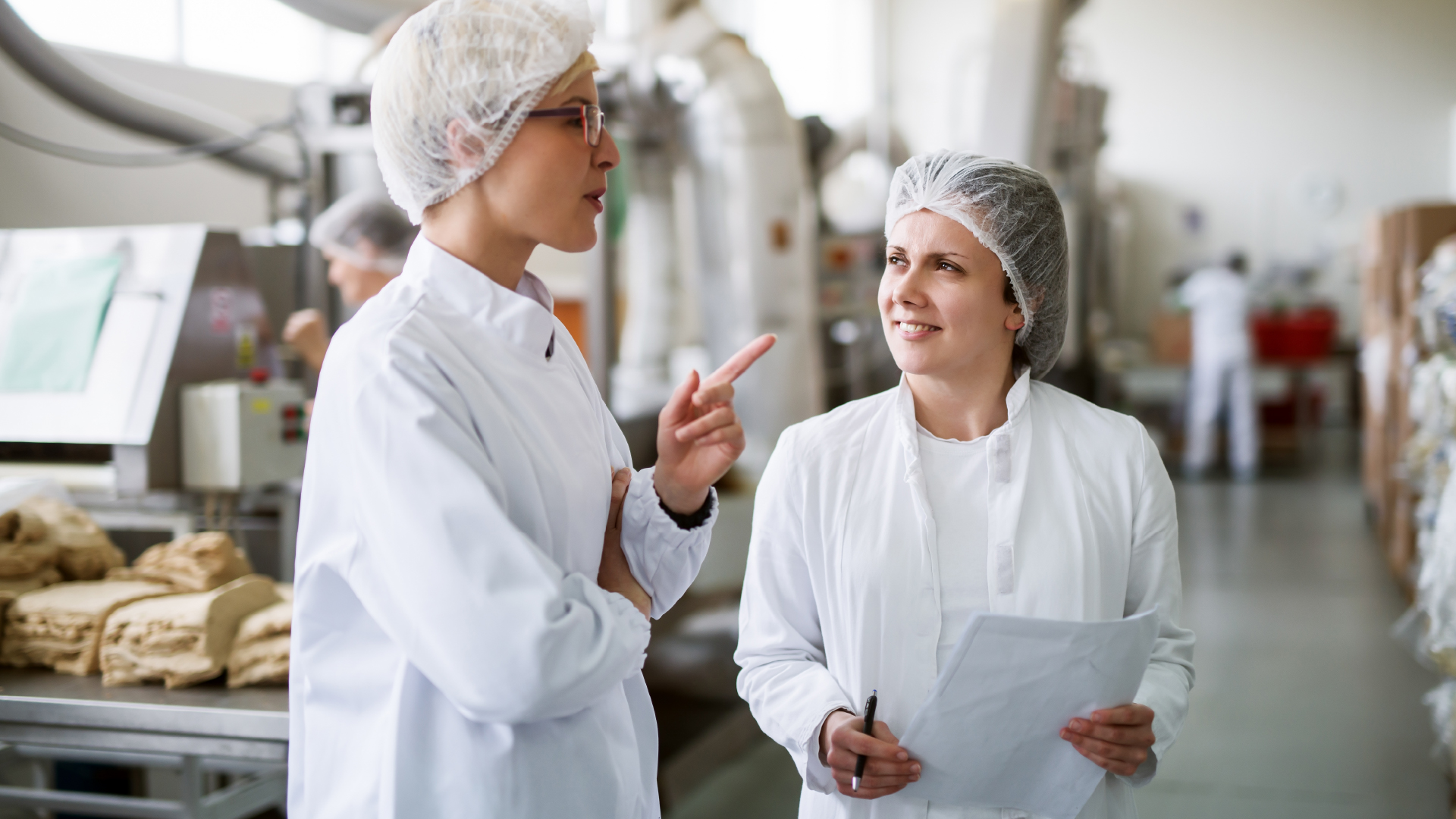 Two female food safety technicians standing and reviewing a report, inside a food manufacturing facility.