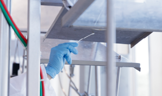 Food safety technician swabbing stainless steel food processing equipment