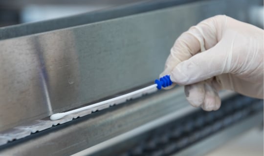 Un technicien utilise un écouvillon de test ATP Neogen® Clean-Trace® sur un convoyeur alimentaire.