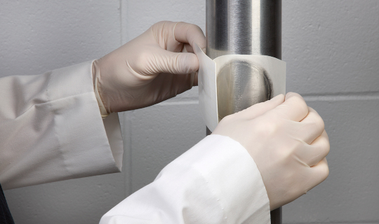 Un technicien de laboratoire applique une plaque Neogen® Petrifilm® Rapid sur un tuyau pour tester la contamination environnementale.