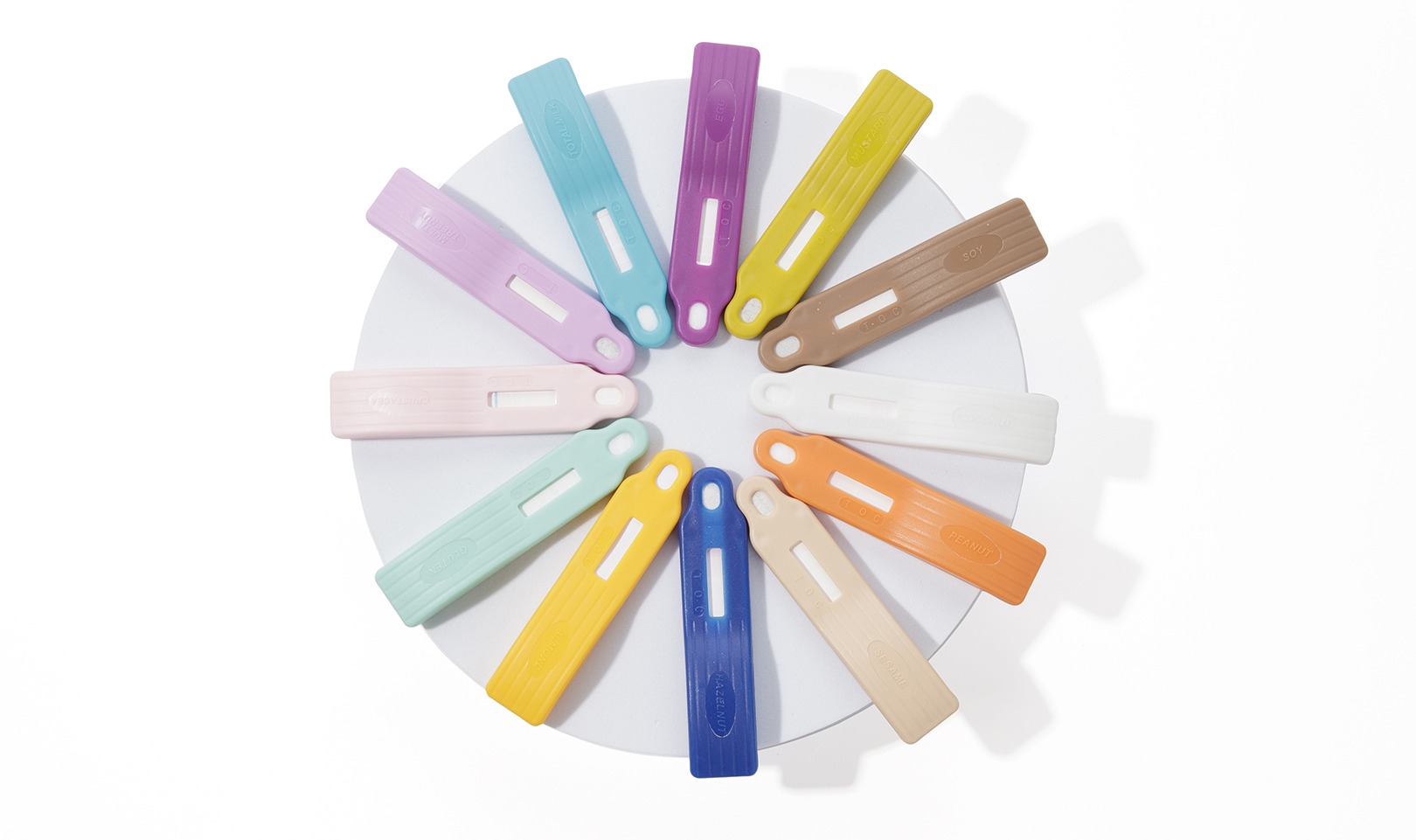 Color-coded Reveal® 3-D allergen lateral flow test devices arranged in a circle on a white background, used for rapid food allergen testing.