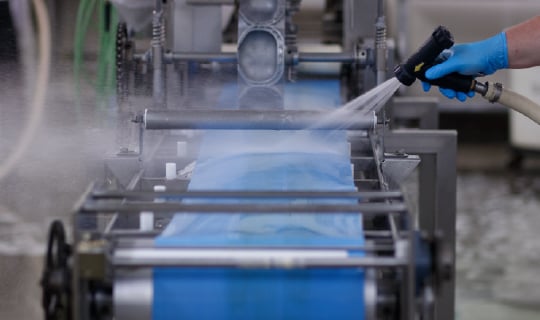 Food safety technician spray cleaning a production packaging line