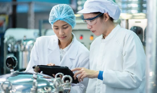 Two food production workers are reviewing data in a food processing facility, demonstrating the application of education in food safety and quality management.