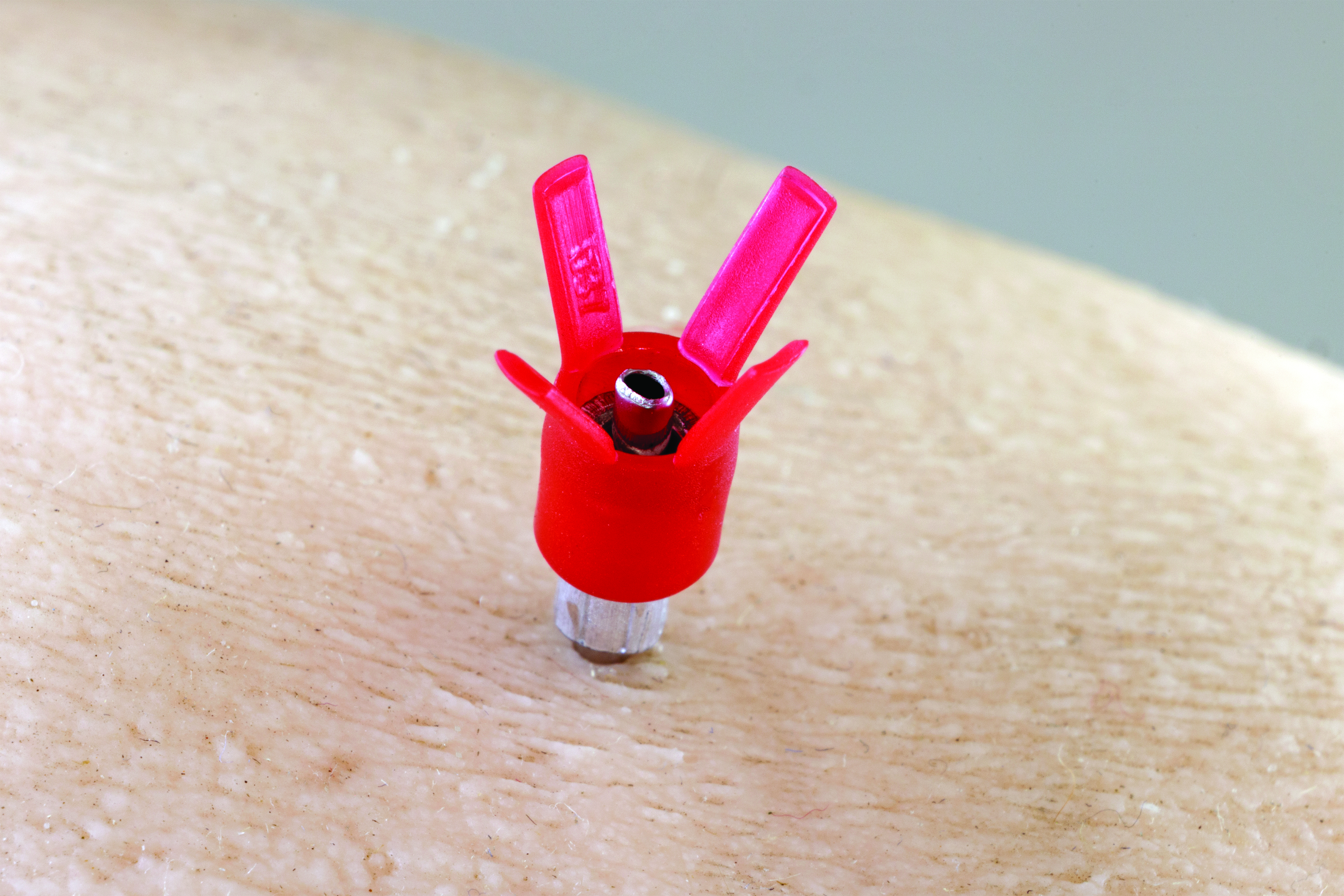 Close-up of a D3X™ needle in use, showing the red X-shaped plastic hub clearly visible against the skin.